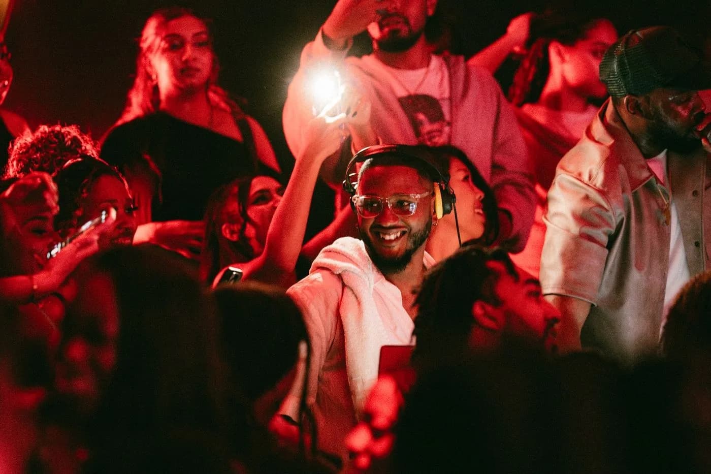 DJ Trizzy in headphones, smiling, surrounded by the crowd under red light